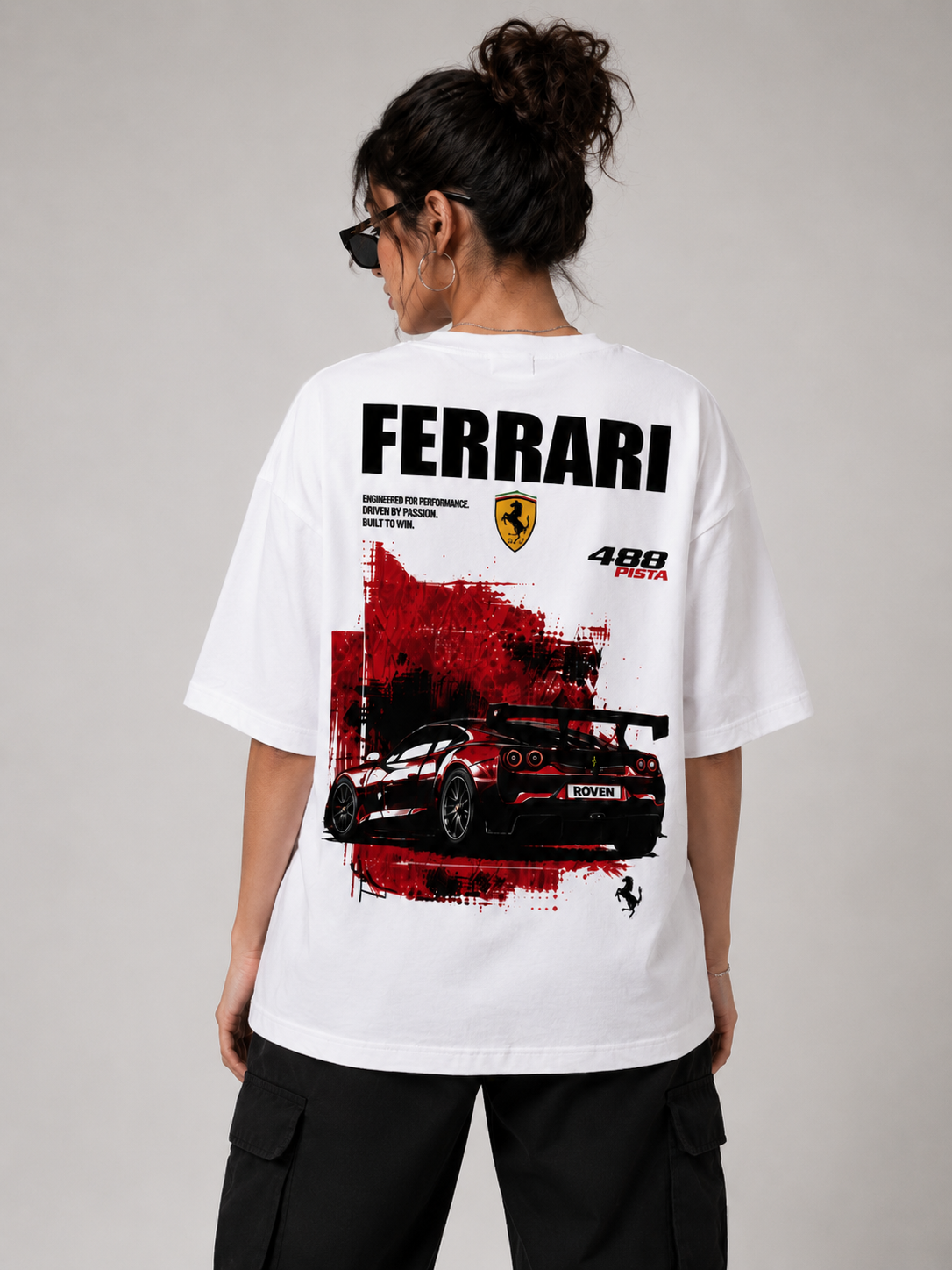 A woman shown from the back wearing a white oversized T-shirt with a large Ferrari racing graphic print on the back, paired with black cargo pants against a light gray studio background.