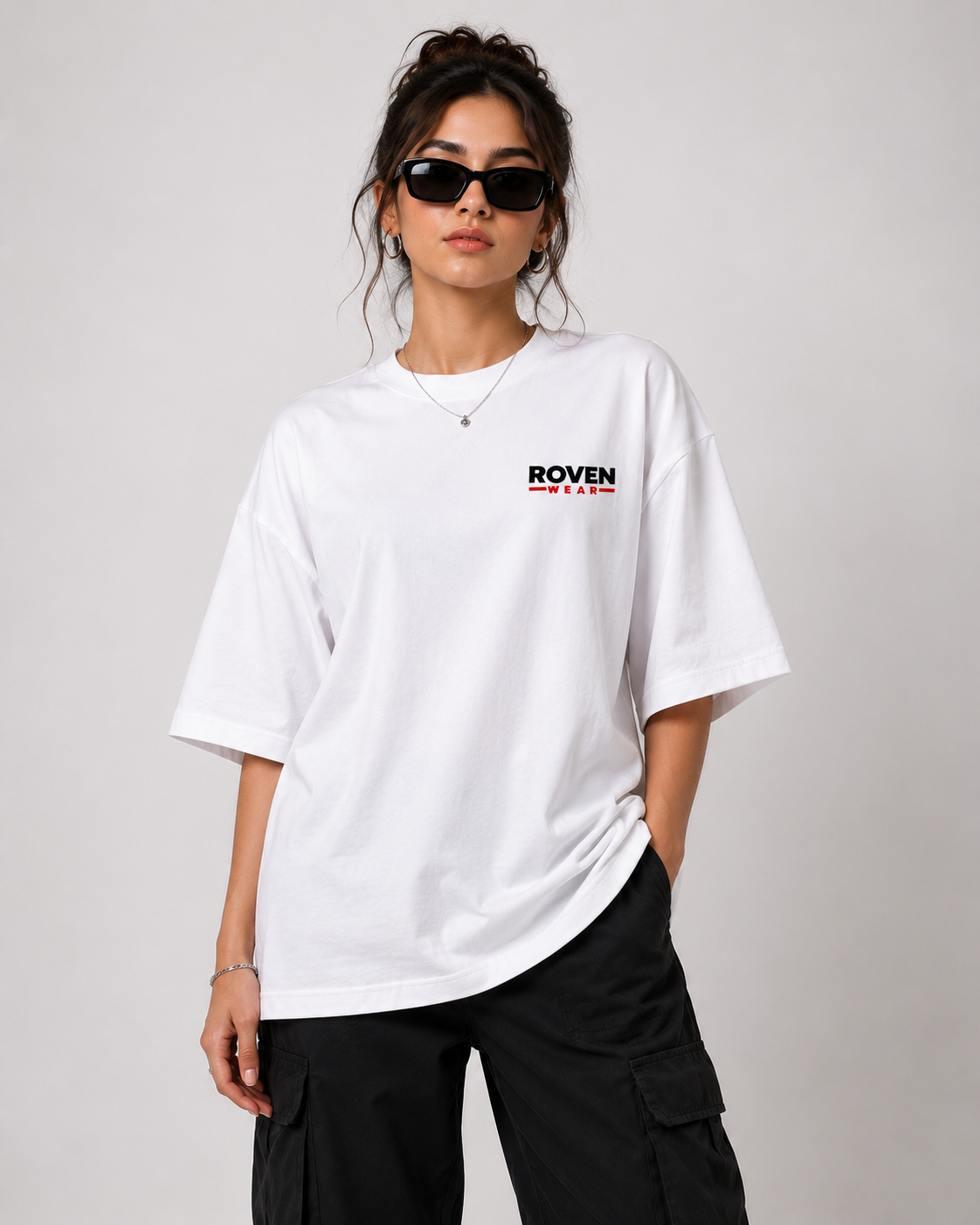 A woman modeling an oversized white t-shirt with a black and red 'ROVEN' logo on the left chest, paired with black cargo pants against a light gray studio background.