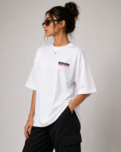 A woman wearing an oversized white t-shirt with a small 'ROVEN' graphic on the chest, paired with black cargo pants, sunglasses, and a gold necklace, posed against a neutral gray background.
